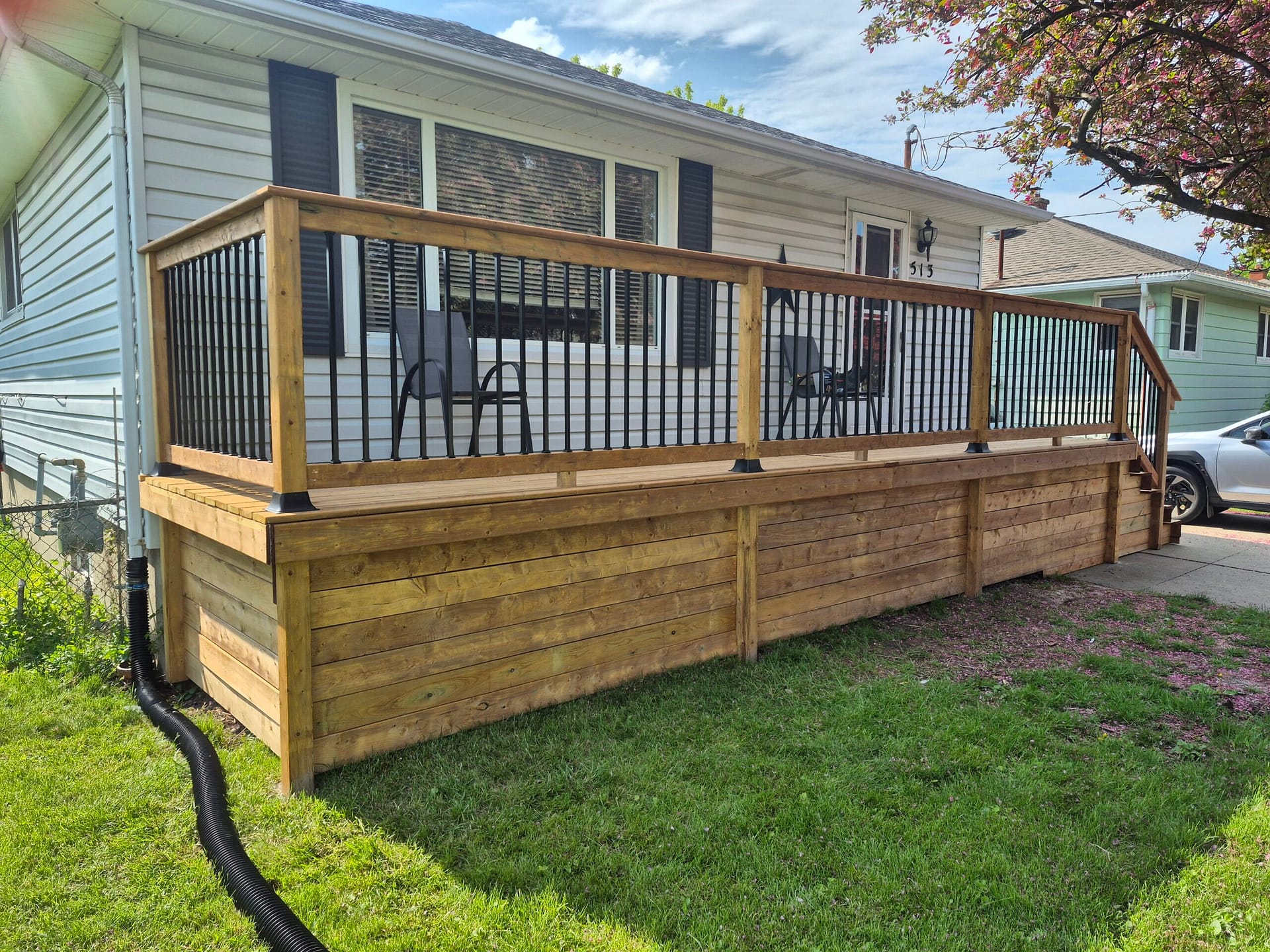 Cedar deck with black metal railing and skirting built onto the side of a house